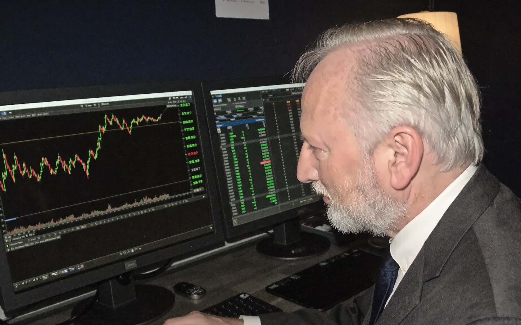 Ian Harvey at his research desk, seen from the side, screens glowing in a dark room